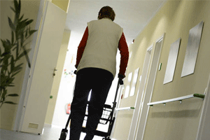 A care home resident walks with a frame