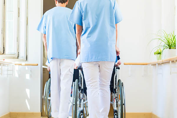 Nurses pushing seniors in wheelchair thru nursing home